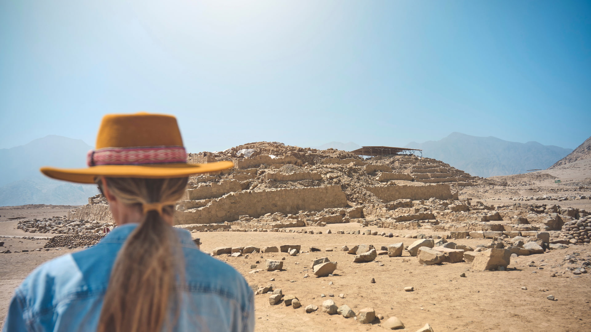 Traveler wearing a hat looks upon the main pyramid during the Tour to Caral from Lima, discovering the oldest city in the Americas - Aremika Travel